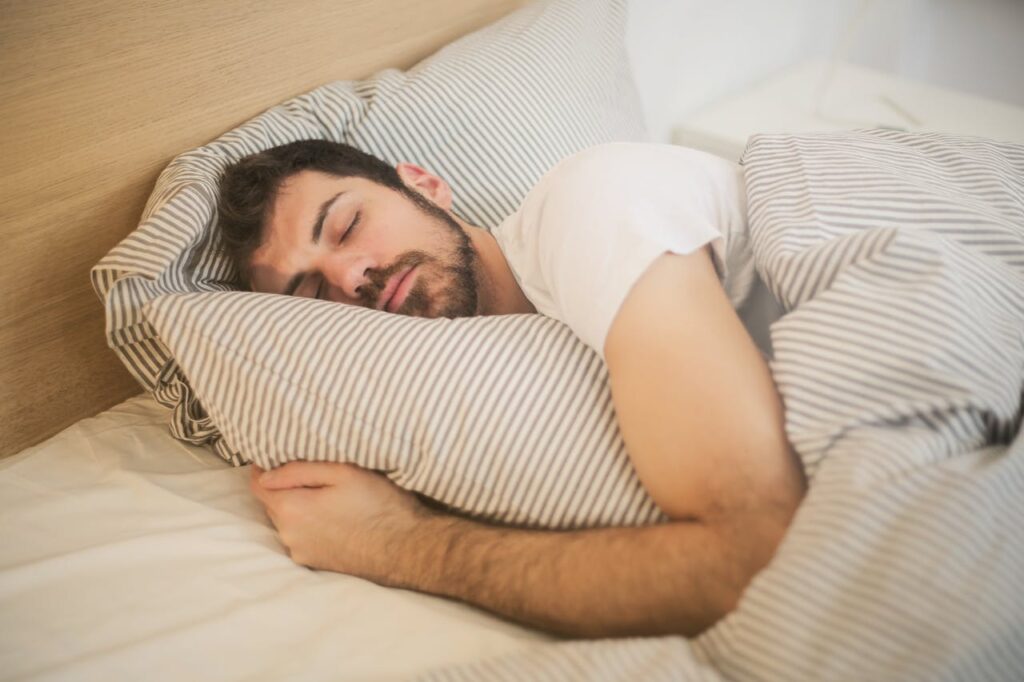 Uomo che dorme serenamente a letto in una stanza luminosa, simbolo di riposo profondo e benessere ormonale naturale.