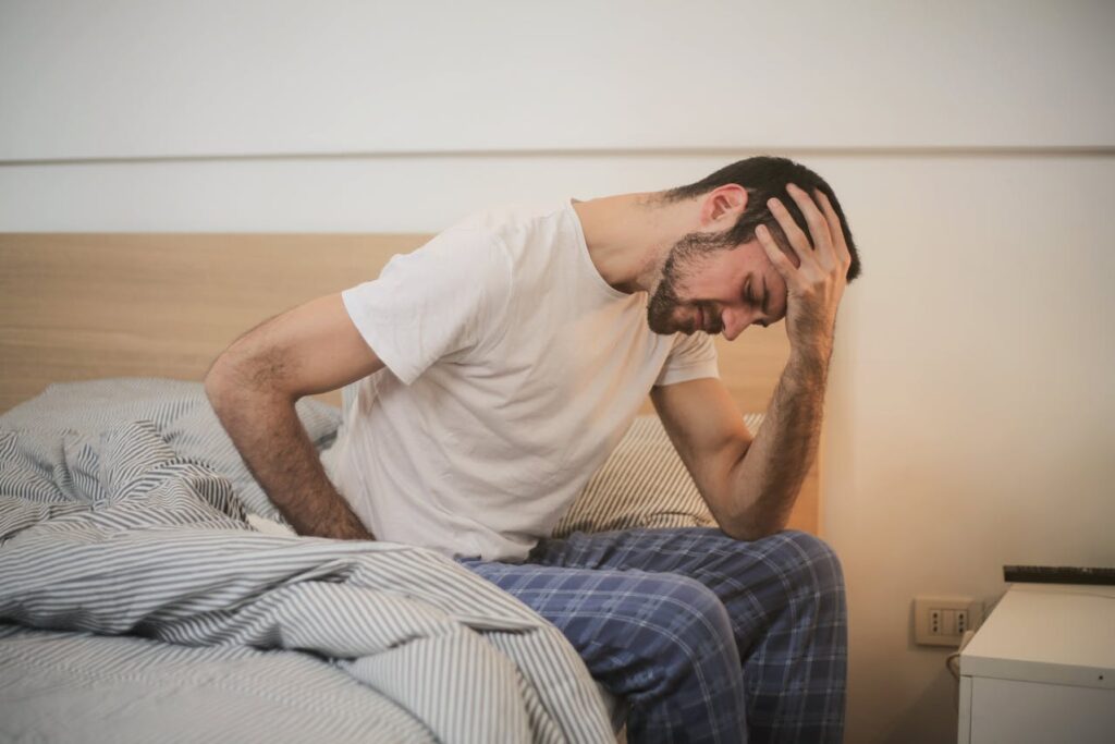 pexels-olly-3771115 Uomo seduto sul letto con espressione sofferente, simbolo di fastidi notturni e sintomi urinari legati alla prostata ingrossata.