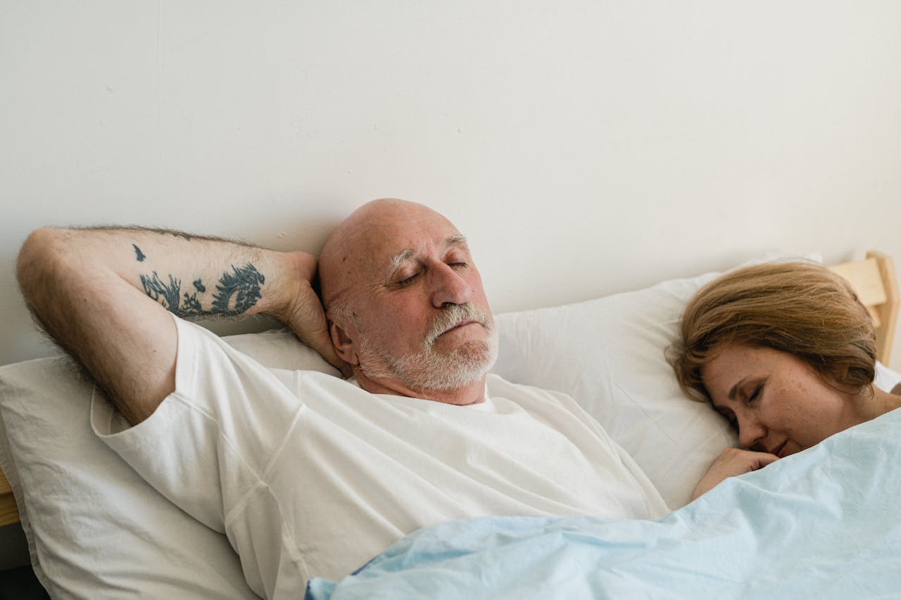 Uomo di 50 anni e donna distesi a letto simbolo di intimità serena e controllo naturale dell’eiaculazione.