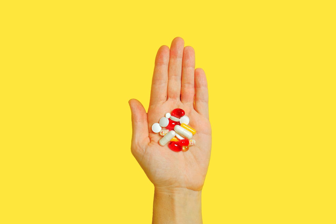 Mano aperta con diverse pillole colorate su sfondo giallo, simbolo della scelta tra farmaci come Tadalafil e Sildenafil.