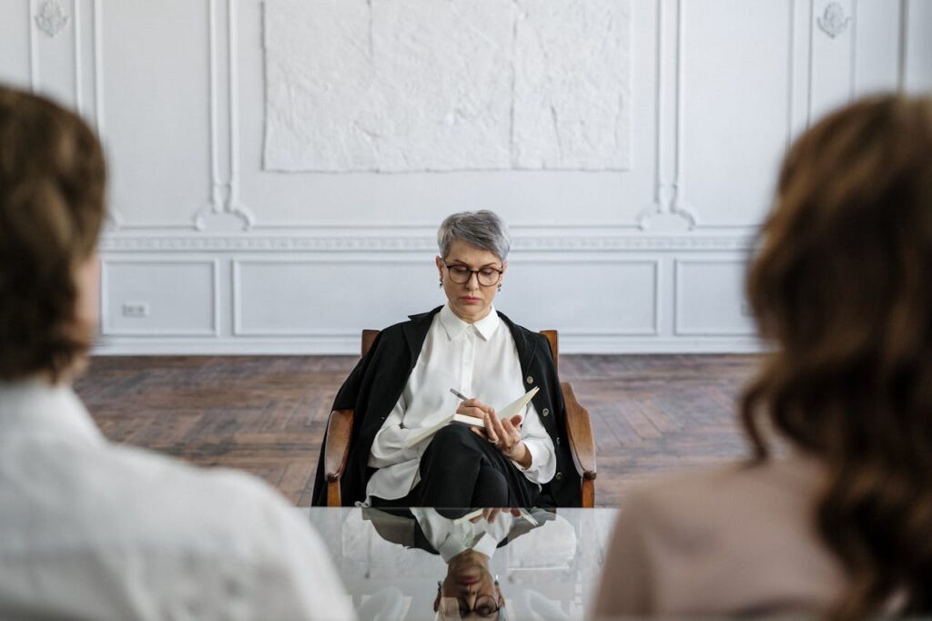 Psicologa professionista che ascolta con attenzione una coppia di mezza età in terapia, facilitando il dialogo e la comprensione reciproca.
