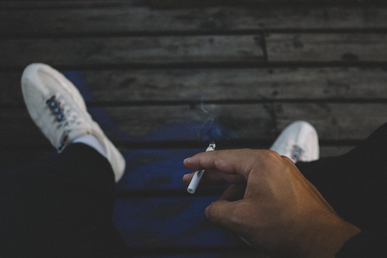 Uomo di mezza età che fuma una sigaretta, con espressione pensierosa e sfondo sfocato.