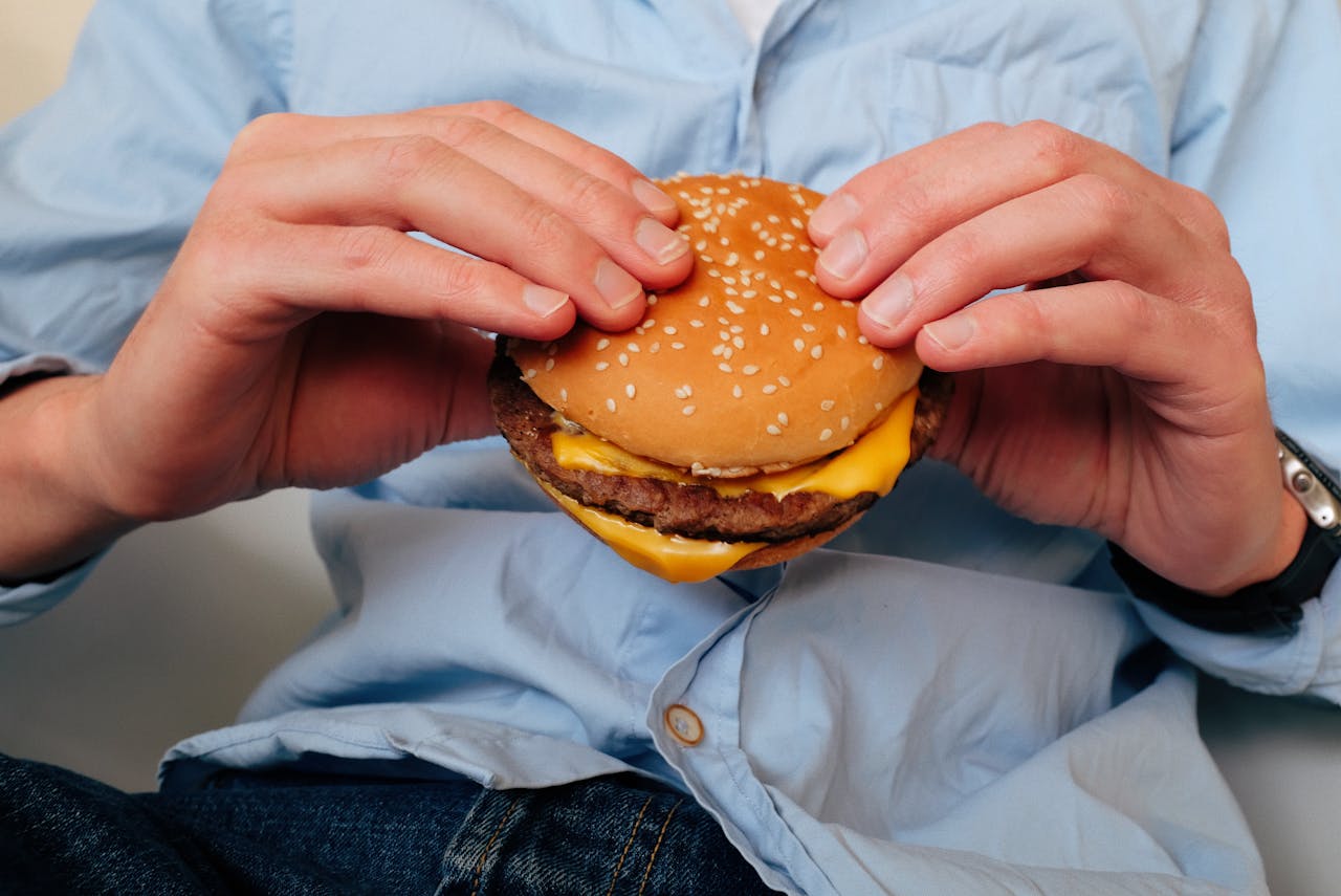 Uomo adulto che tiene un hamburger fast food, esempio di alimenti che fanno male alla salute se consumati frequentemente.